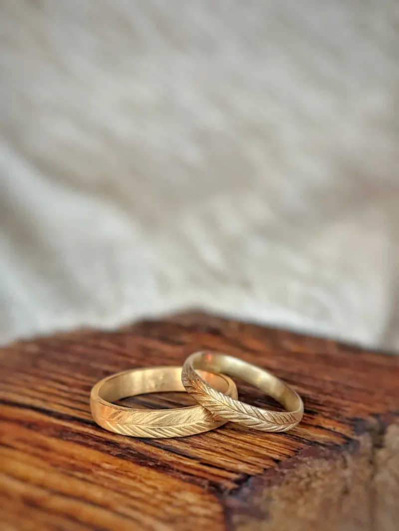 Immergrün Eheringe - fein matte Ringe mit gesägtem Kiefernzweig aus 750 und 585 Gelbgold auf Holz liegend