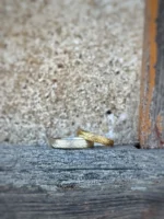 Immergrün Eheringe - fein matte Ringe mit gesägtem Kiefernzweig aus 750 und 585 Gelbgold auf rustikalem Balken