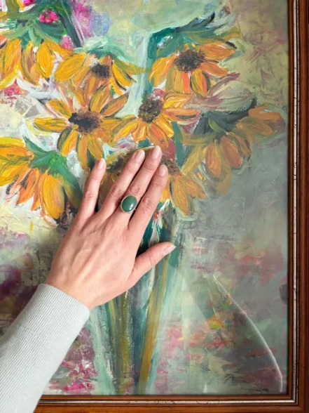 Gelbgoldener Ring mit großem, ovalen grünen Edelstein Aventurin getragen vor Sonnenblumenbild