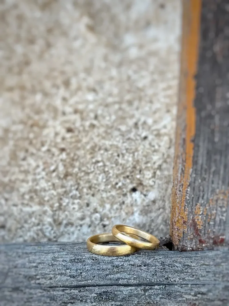 kleine Wellen Eheringe - einzigartige, sanft gefeilte Eheringe aus 750 Gelbgold mit feiner Struktur auf rustikalem Balken