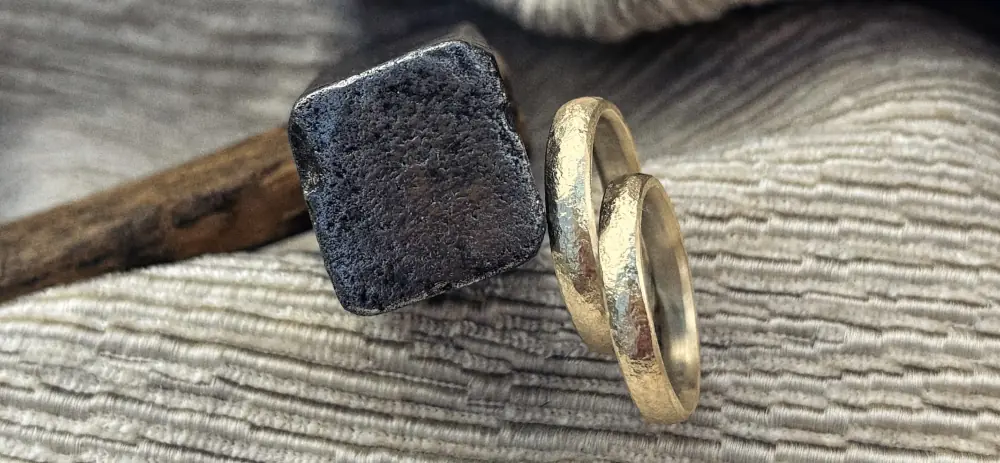 Liebesbrief Eheringe mit einzigartiger geschmiedeter Struktur aus 750 Gelbgold an Hammer lehnend
