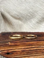 robuste und klassische Sandsturm Eheringe mit grob gefeilter, zerkratzter Struktur aus 750 Gelbgold auf Holz liegend
