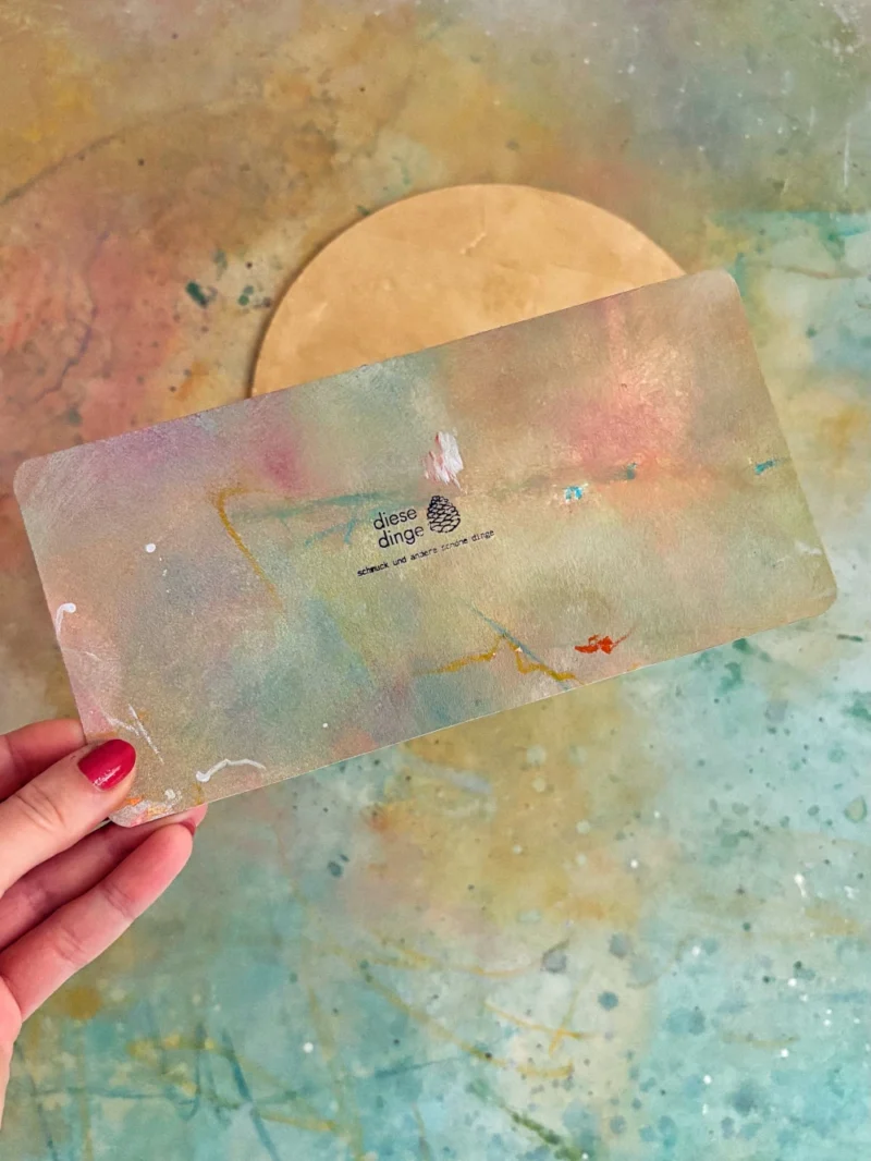 Gutschein Karte künstlerisch bunt gemalt in kräftigen Farben in Hand gehalten